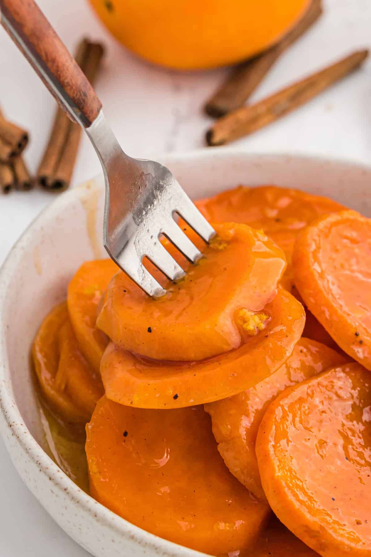 A fork in a bowl of sliced baked candy yams