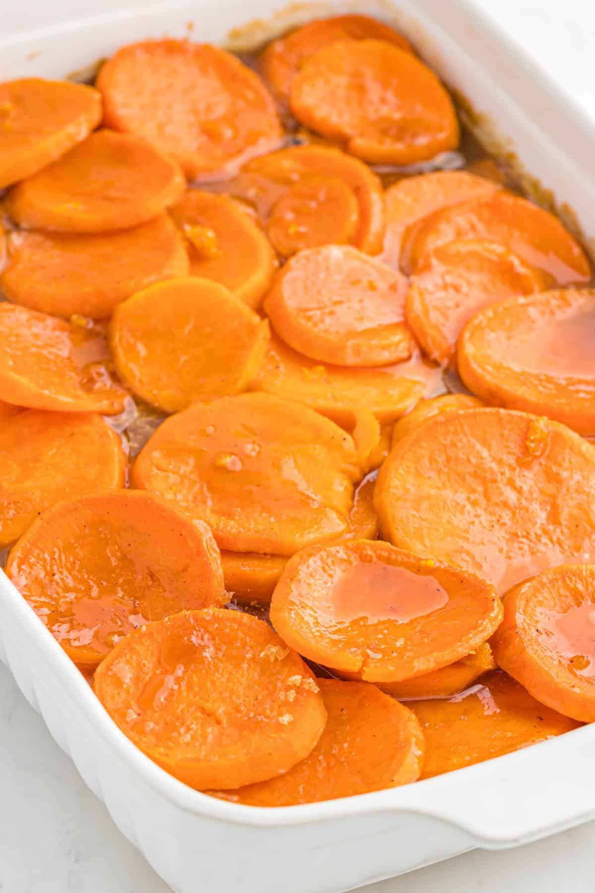 A white baking dish of a sliced candied yams recipe in syrup