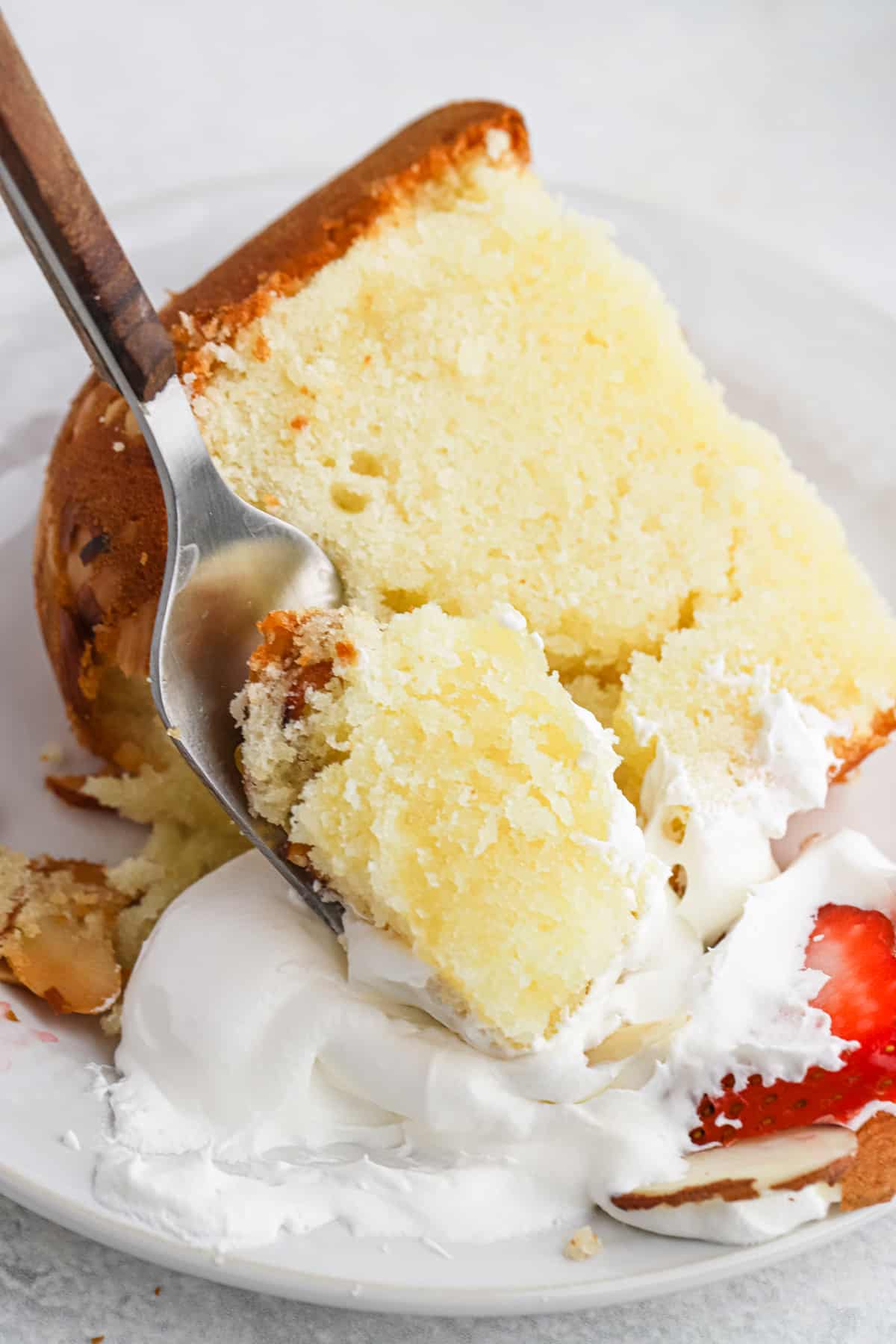 A slice of almond pound cake on a white plate with a fork.
