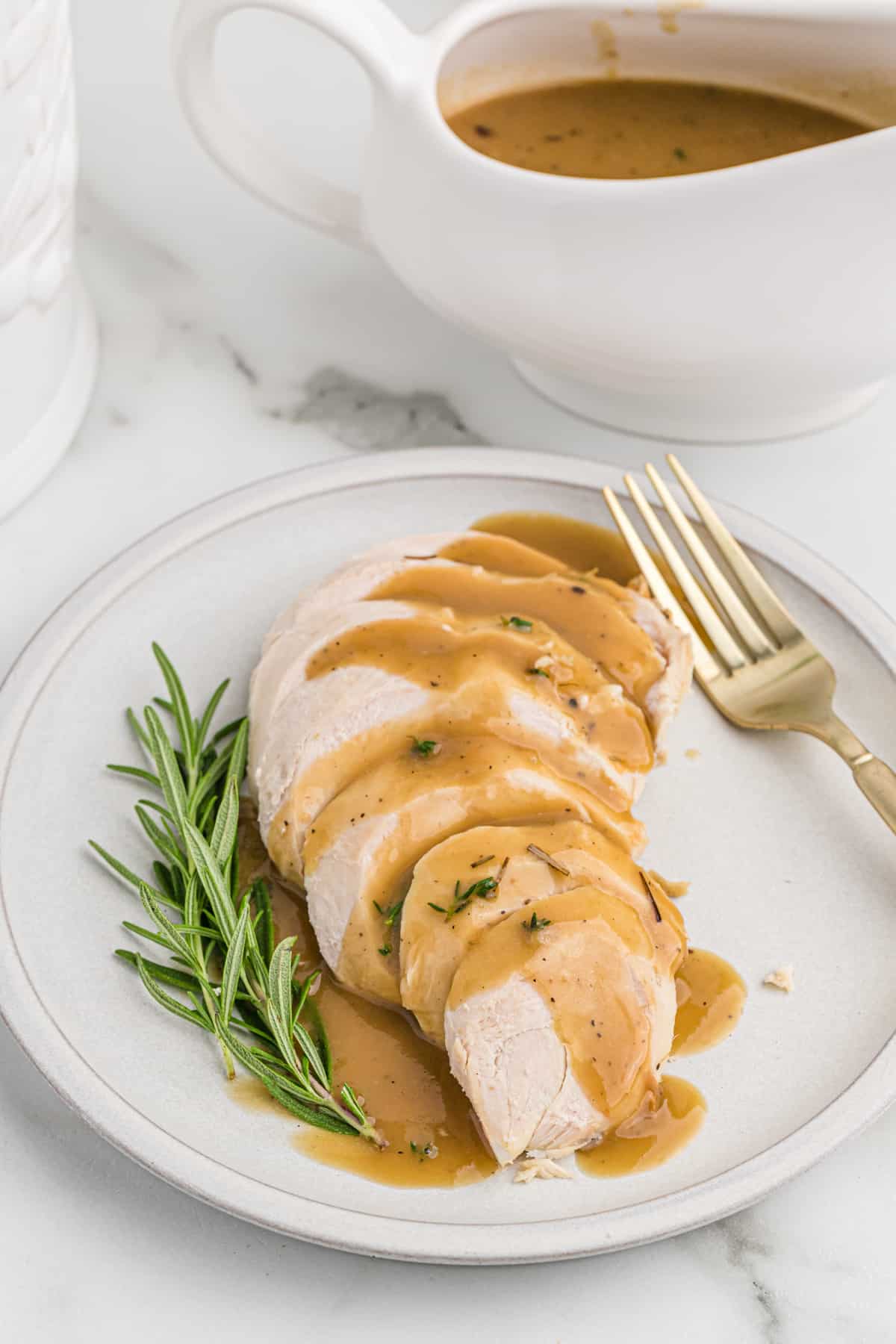 Freshly made turkey gravy from turkey drippings poured over turkey breast slices on a white platter.