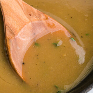 A wooden spoon in a saucepan of turkey gravy.