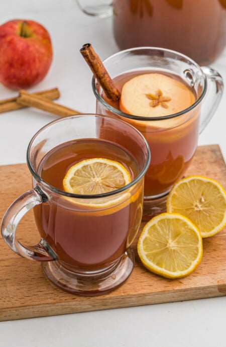 Two mugs of wassail with slices of orange and apple floating on top.