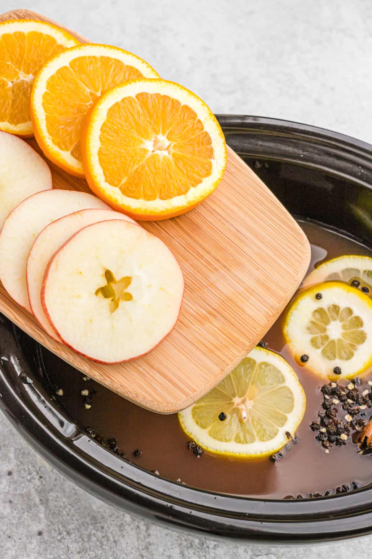 Sliced apples and oranges being eased into a crockpot of wassail.