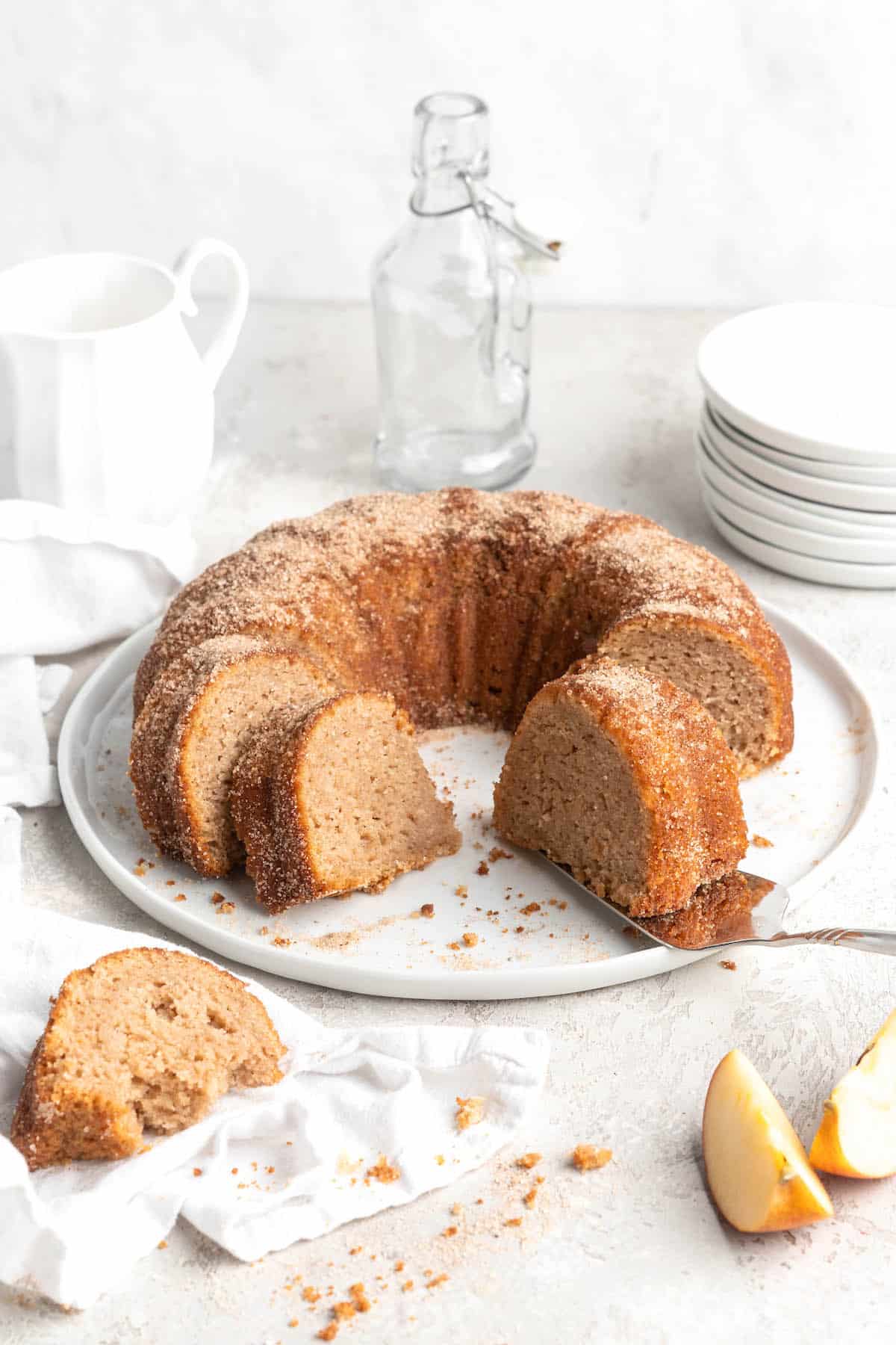 Slices of an apple cider donut cake recipe against a white background with white plates in the background