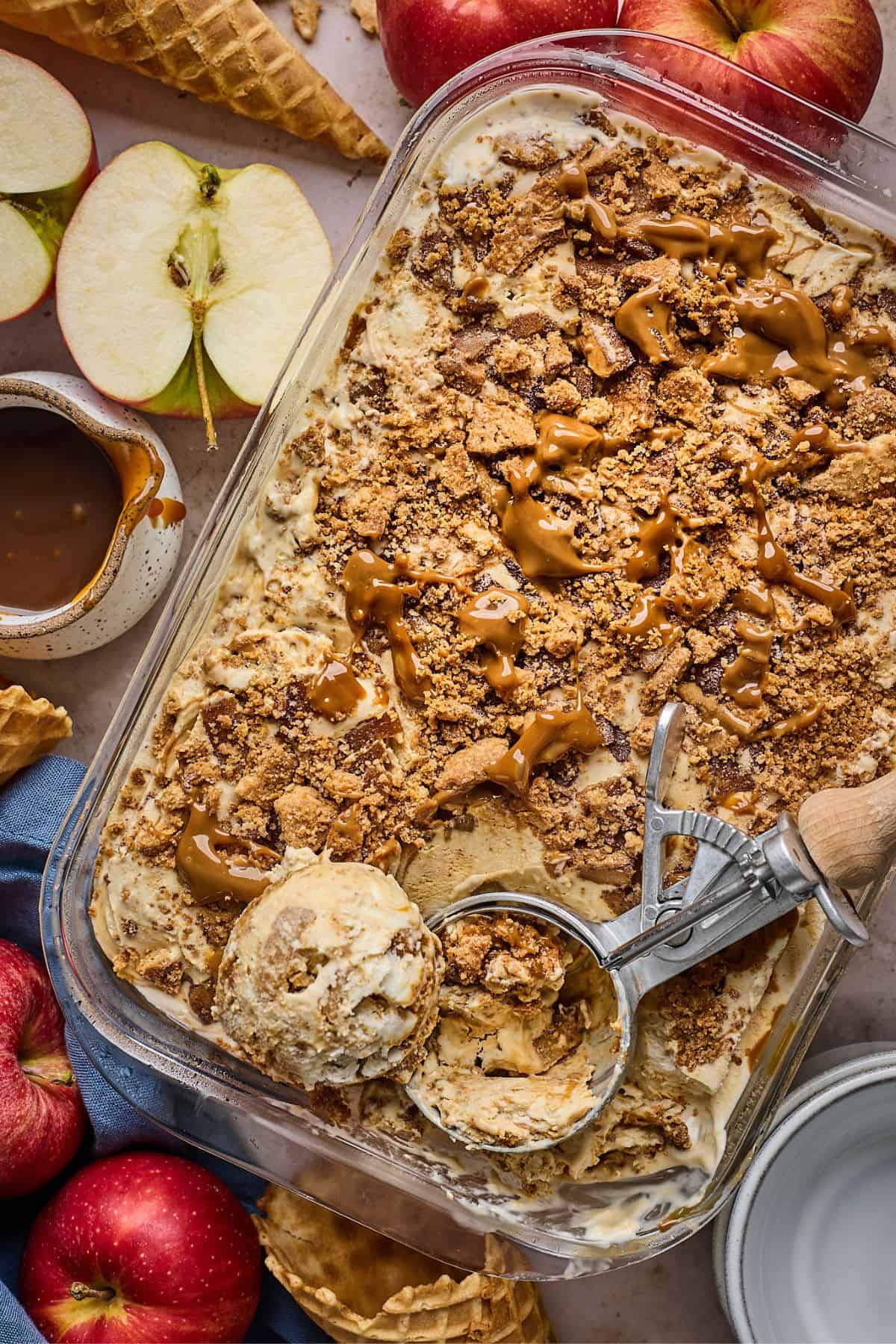 Container full of apple pie ice cream with an ice cream scoop and a scoop of ice cream on top 