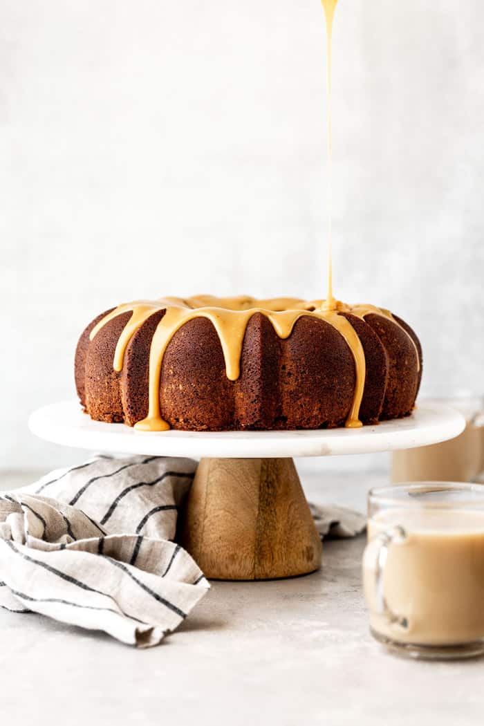 Chocolate bundt cake with caramelized white chocolate ganache glaze on white cake stand with glasses of Irish Cream ready to serve