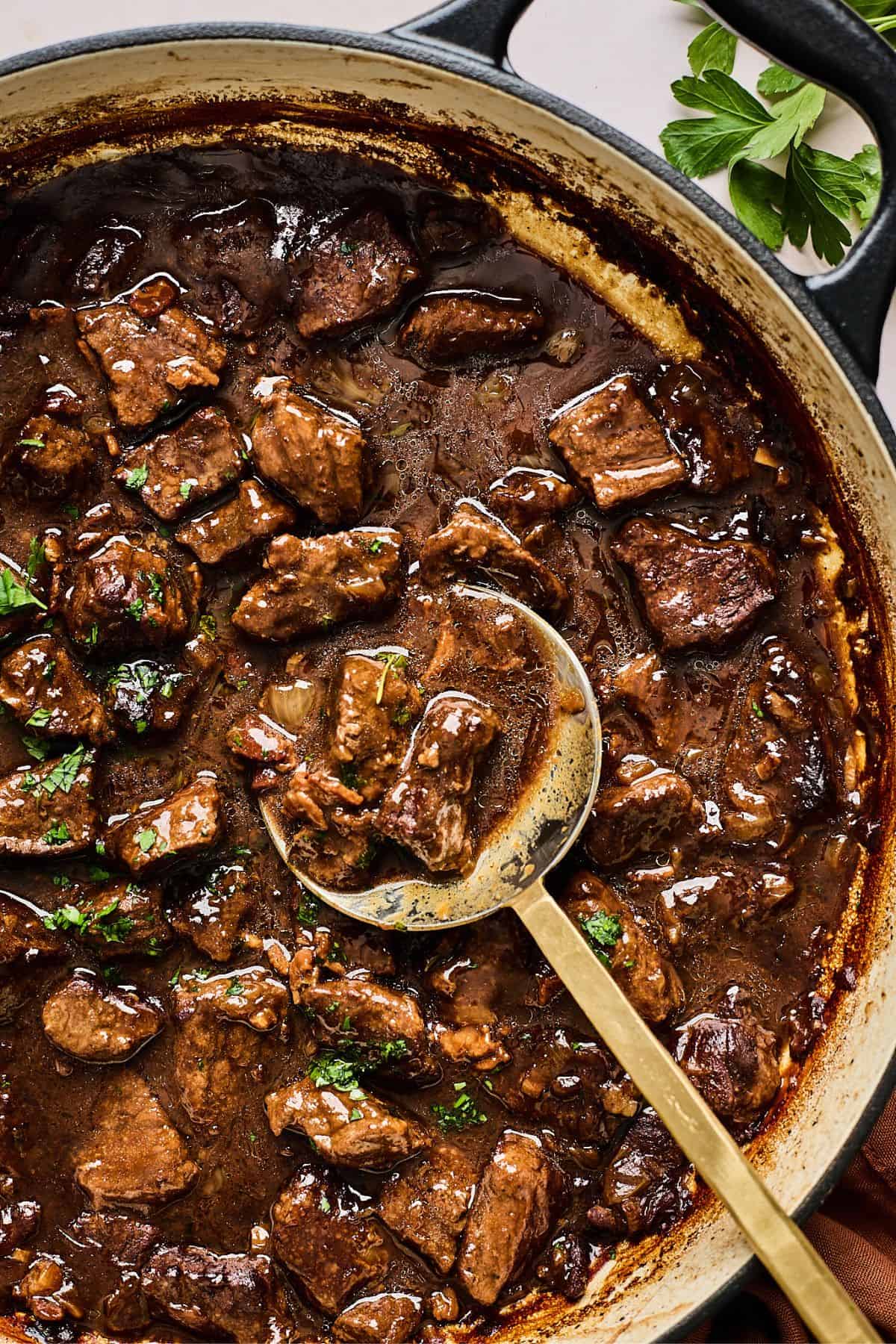 A ladle scooping up beef tips from a large pot