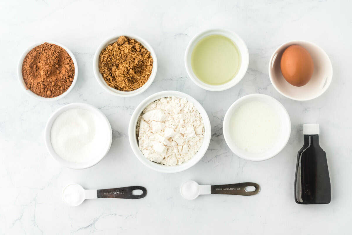 dry ingredients, buttermilk, egg and vanilla in white bowls on a white background to make a chocolate cupcake recipe