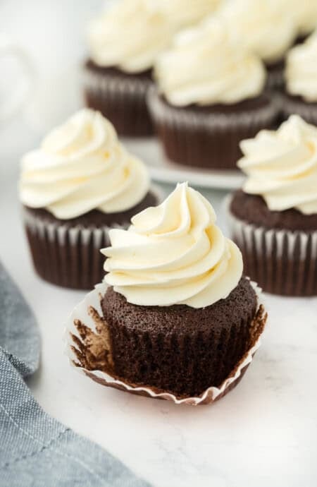 A chocolate cupcake recipe with one having the wrapper down and several in the white background