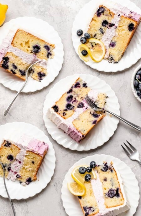 Blueberry lemon layer cake slices on white plates ready to serve with silver forks