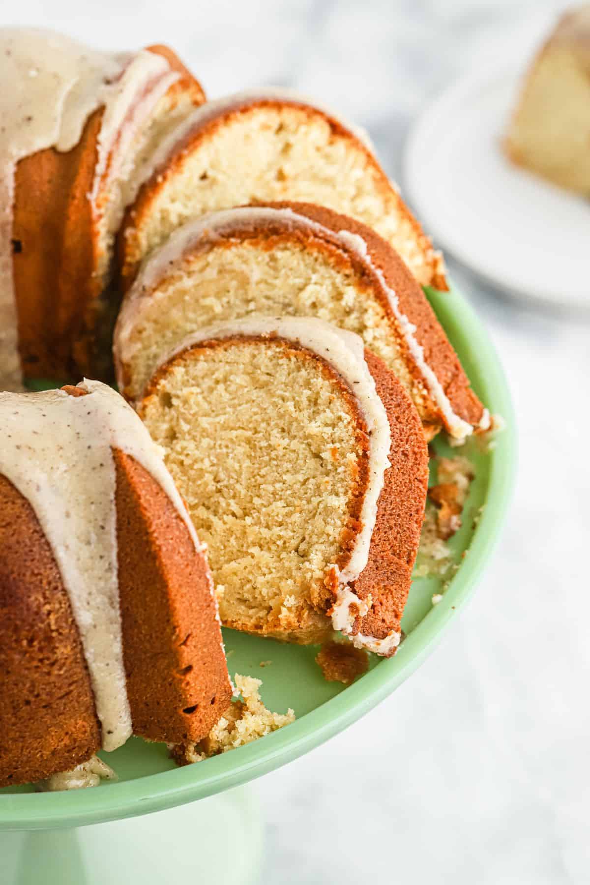 Brown sugar cake with browned butter glaze over the top on a green cake stand with a few pieces sliced and leaning over.
