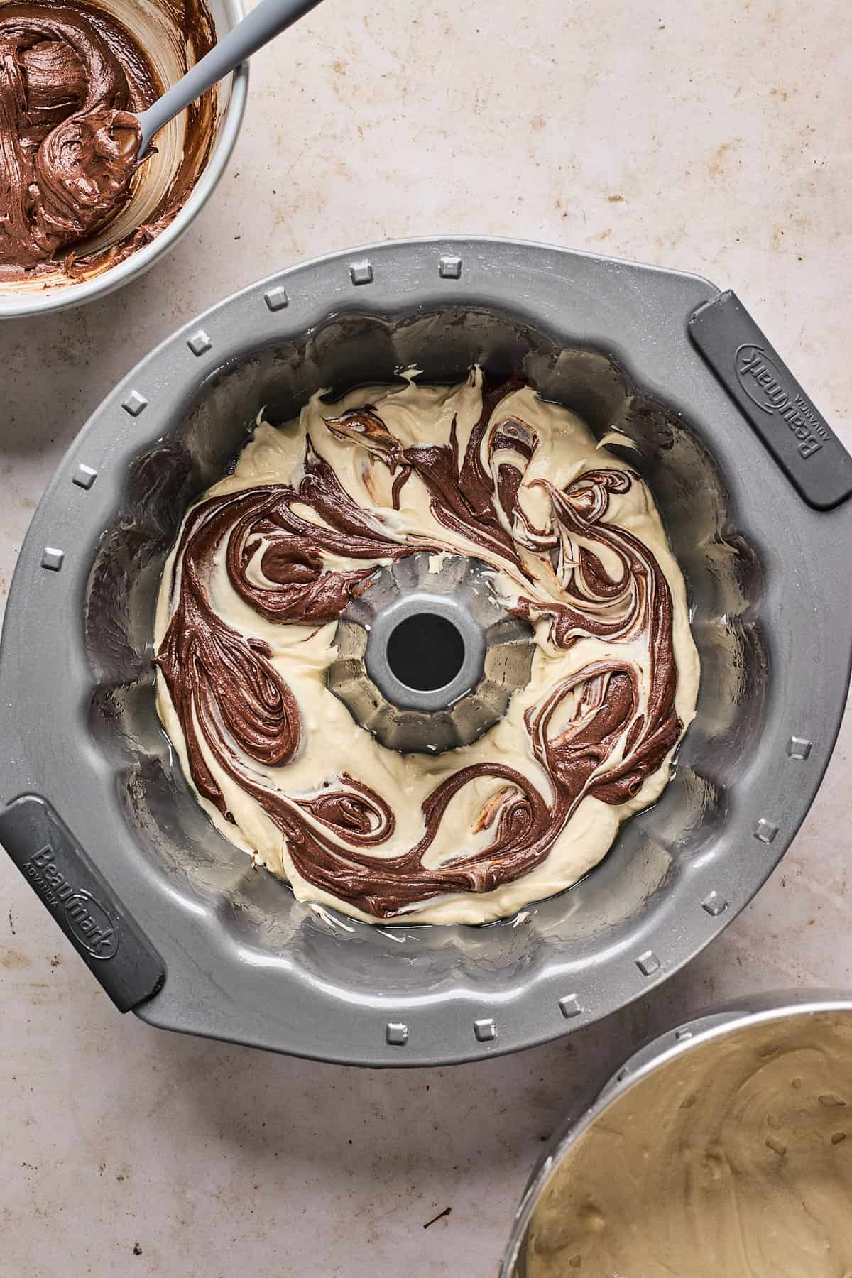 Pound cake being assembled in a bundt pan with two different flavors of cake batter swirled together.