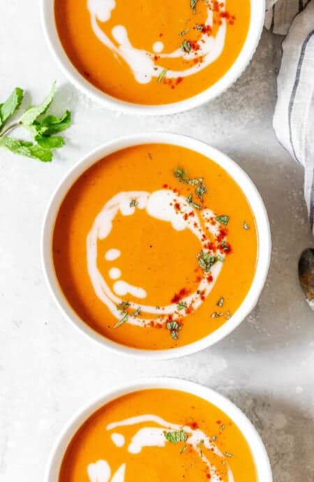 Overhead of Creamy Carrot Soup Recipe in three bowls with spoons and parsley on white background