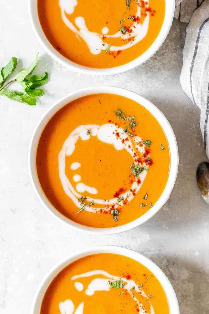 Overhead of Creamy Carrot Soup Recipe in three bowls with spoons and parsley on white background