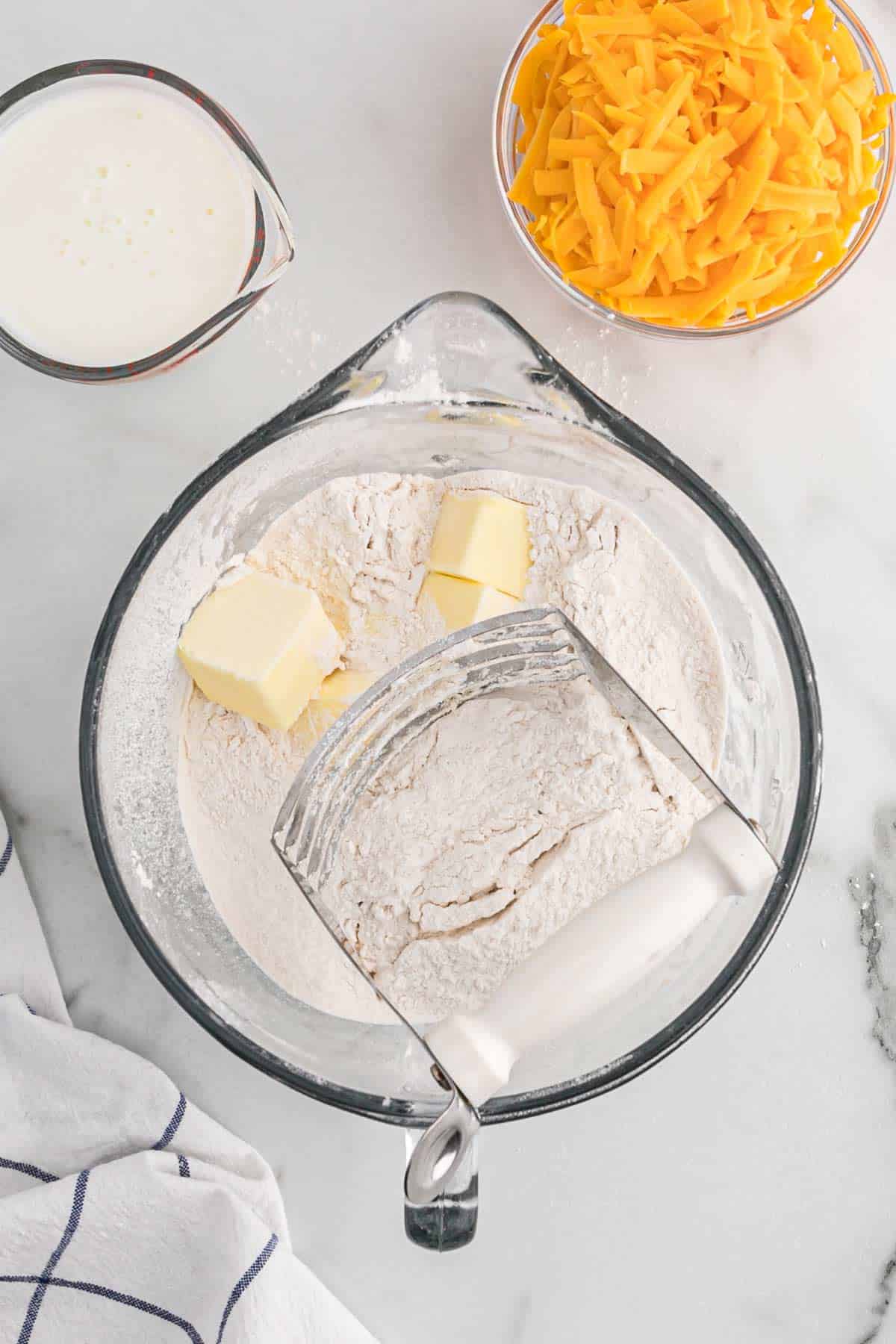 Butter added to the flour mixture and a pastry cutter to the side.