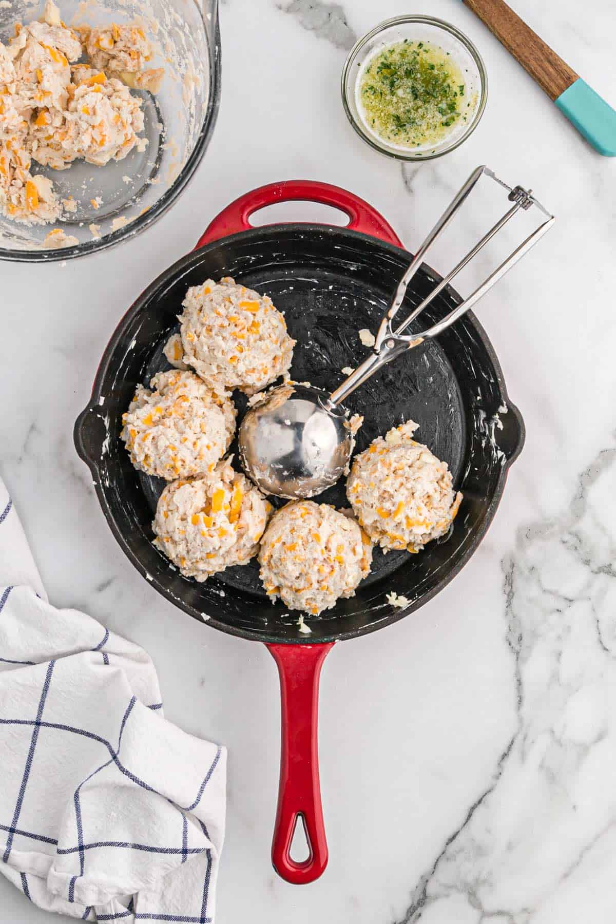 An ice cream scoop placing cheddar bay biscuits in a pan.