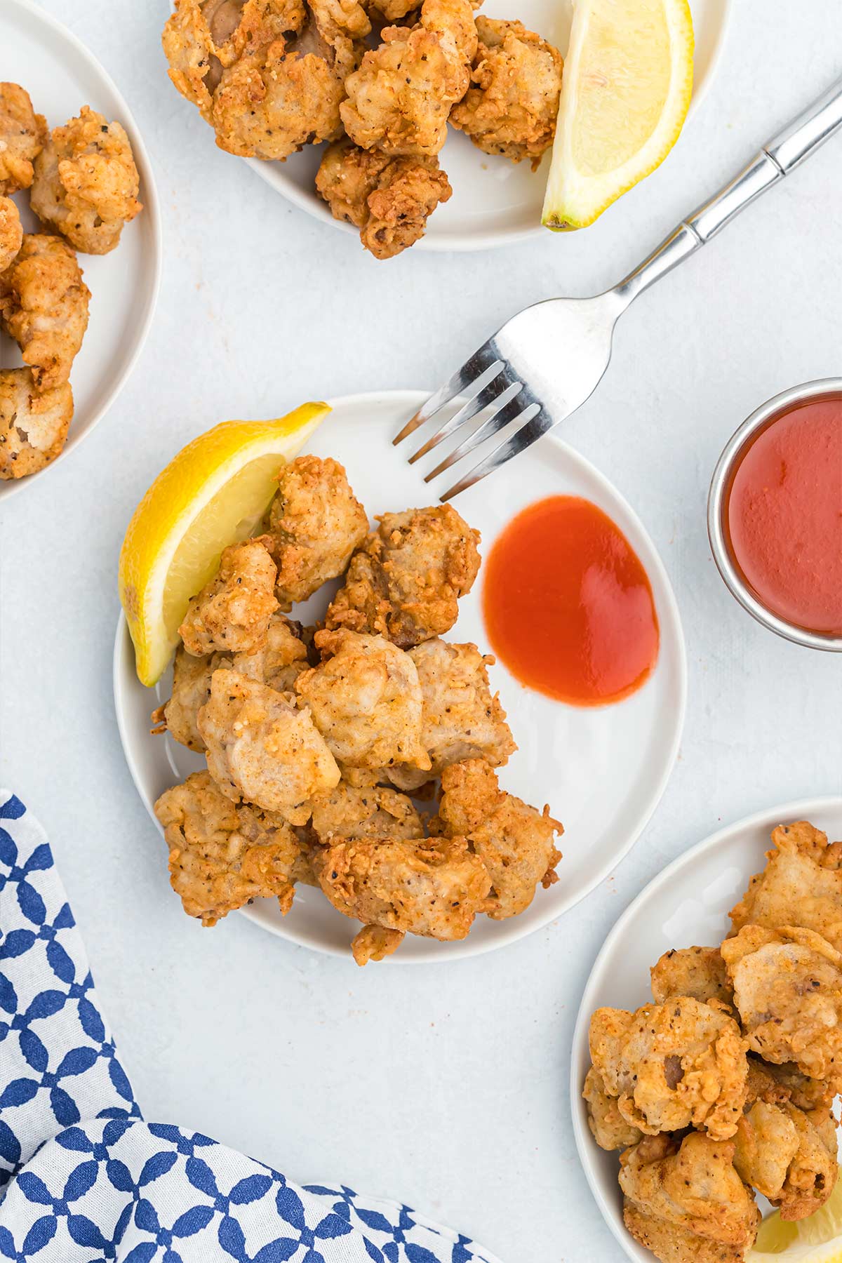 Fried chicken gizzards served up on plates on the white table with side of hot sauce.