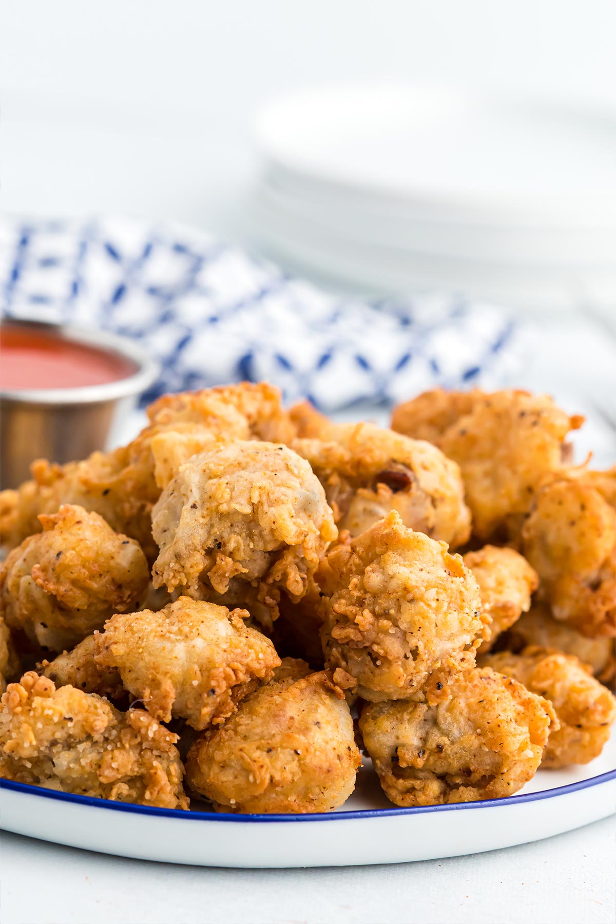 Fried chicken gizzards on a plate with hot sauce in a bowl and blue and white napkin in the white background.