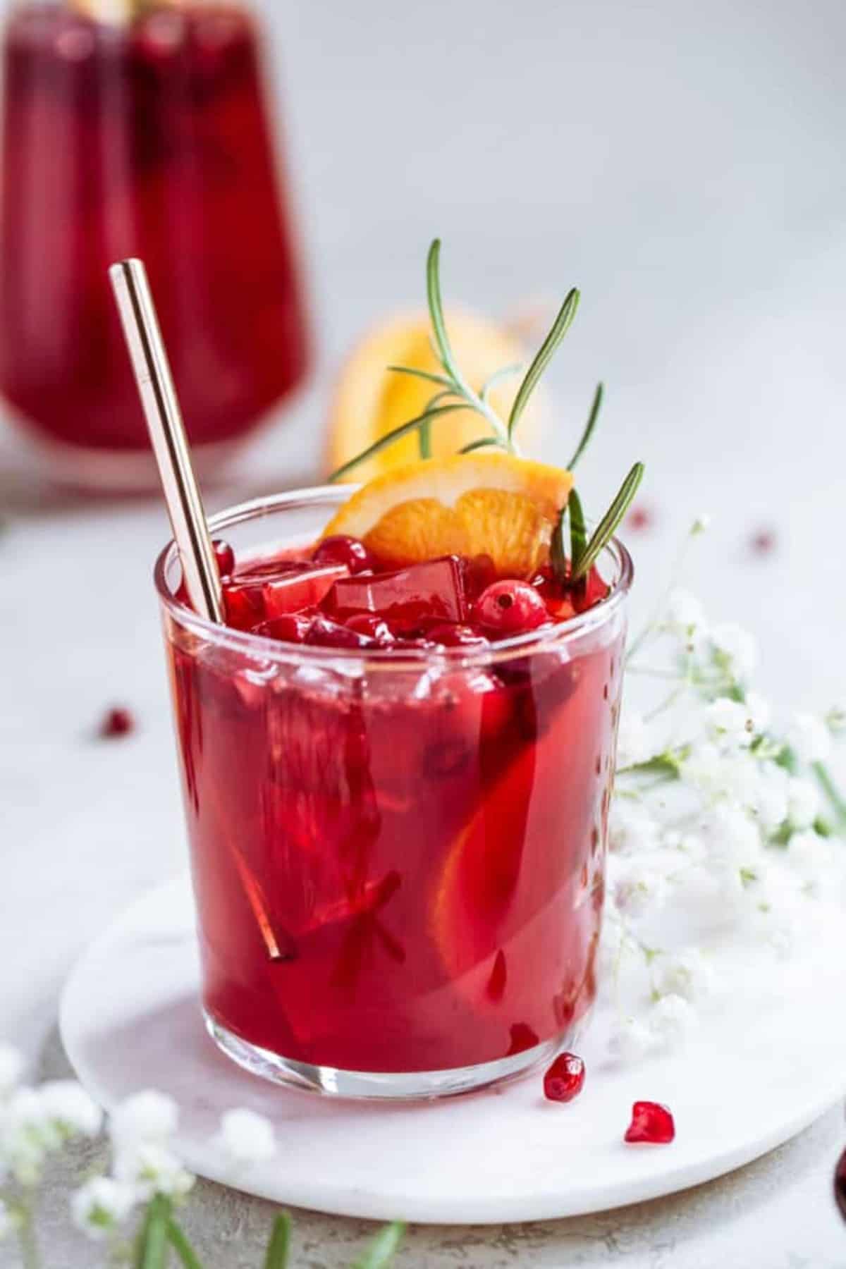 A short glass of punch with a carafe in the background against a white background