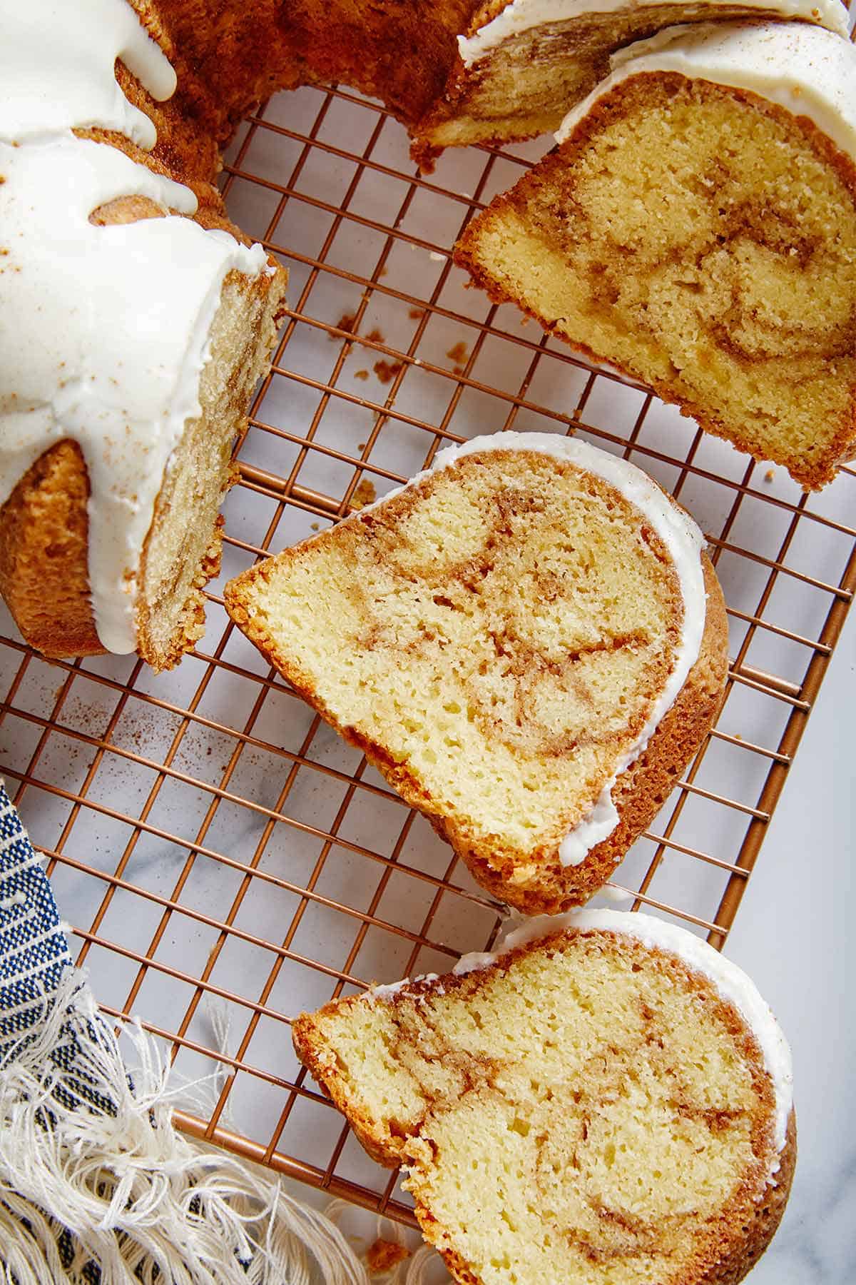 A whole cinnamon roll pound cake on a baking wrap with some of it cut away and several slices laying face up on the rack.