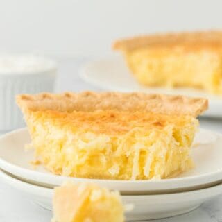 A slice of coconut cake with a piece being eaten on a fork in a white background