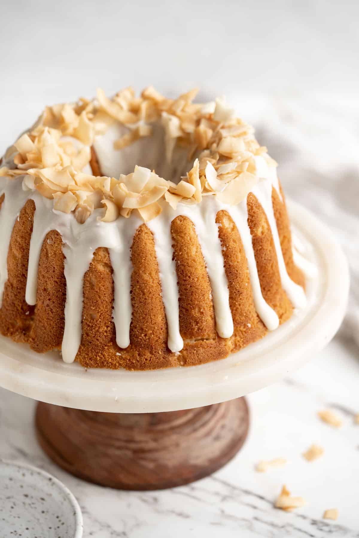 Coconut pound cake on a white cake stand with glaze and coconut flakes on top