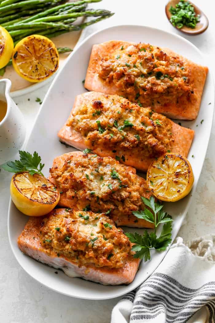 A crab stuffed salmon recipe on a white platter with lemon wedges and herbs ready to serve