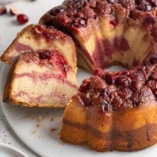 slices of cranberry bundt pan on a white plate on a white background with cranberries on the background