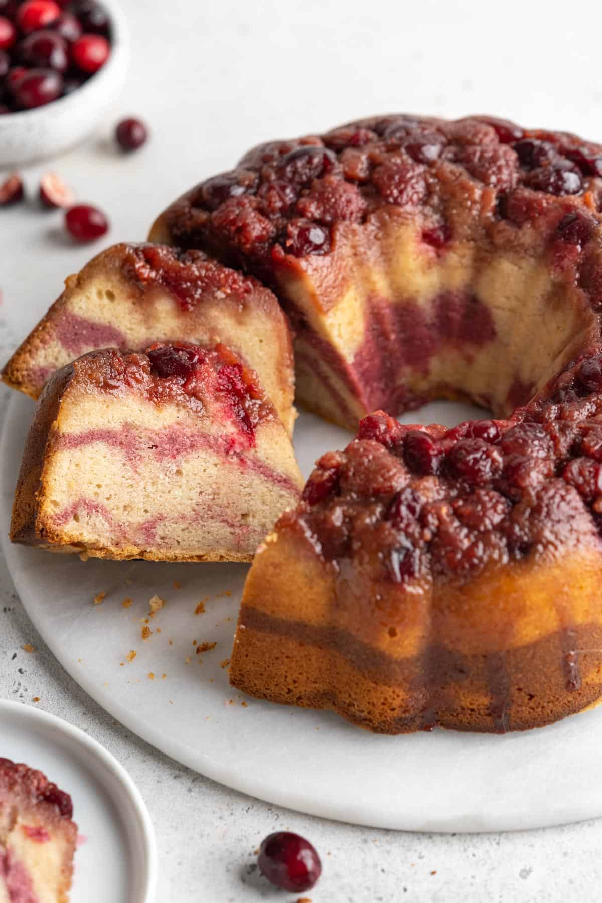The cranberry bundt cake recipe with slices cut out of it and leaning over on the platter.