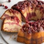A cranberry bundt cake on a platter with a couple slices cut and laying over on the side.