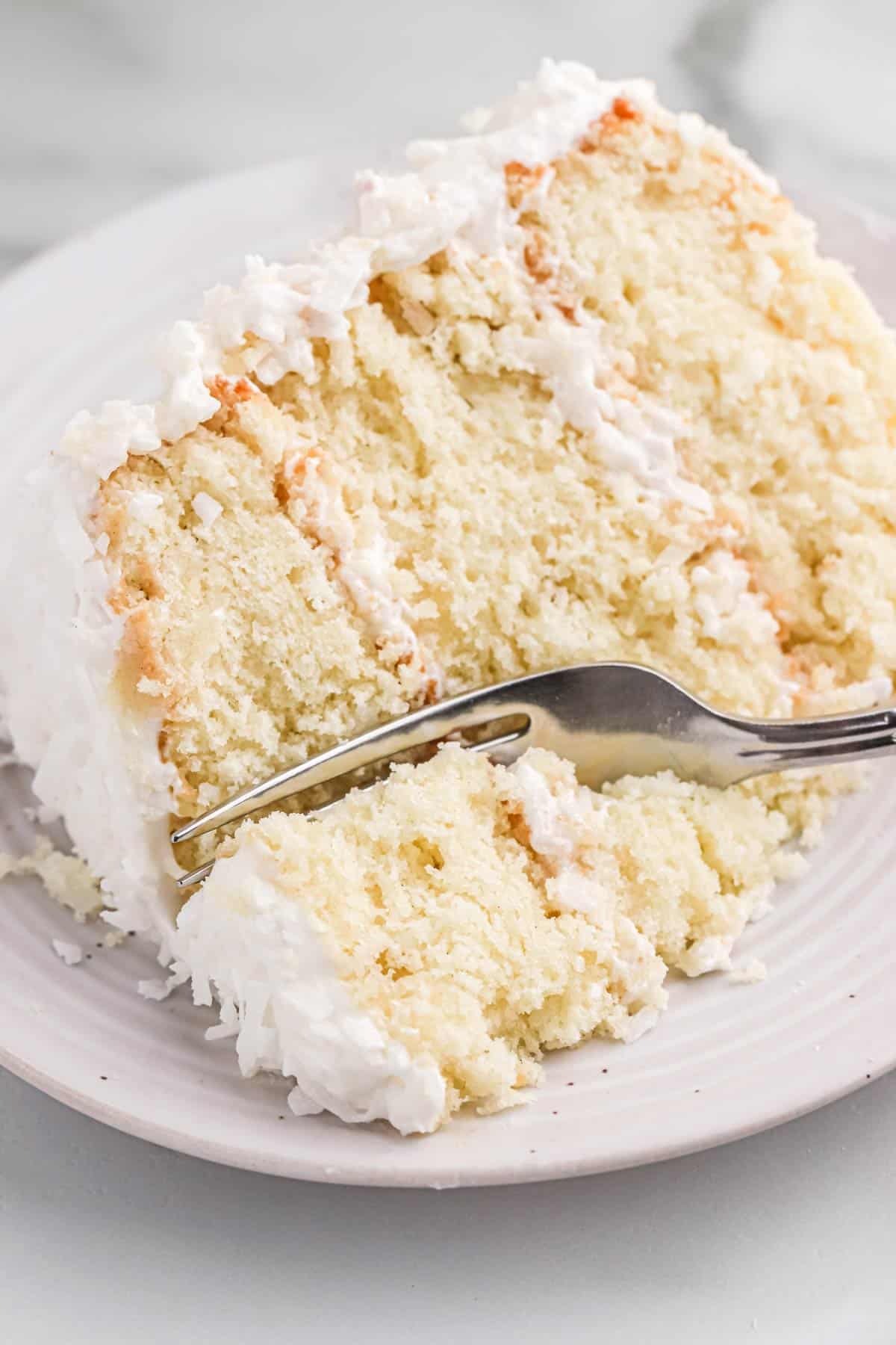 A fork cutting into a piece of old fashioned coconut cake to take a bite.