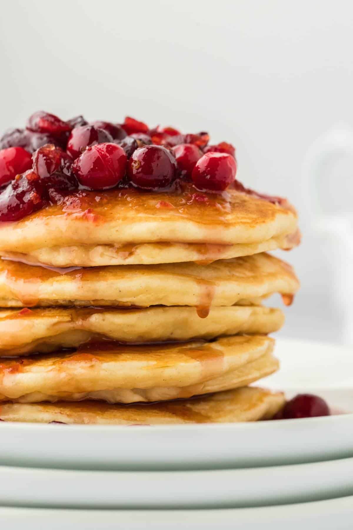 Eggnog Pancakes stacked on a white plate topped with Cranberry Maple Syrup ready to serve.