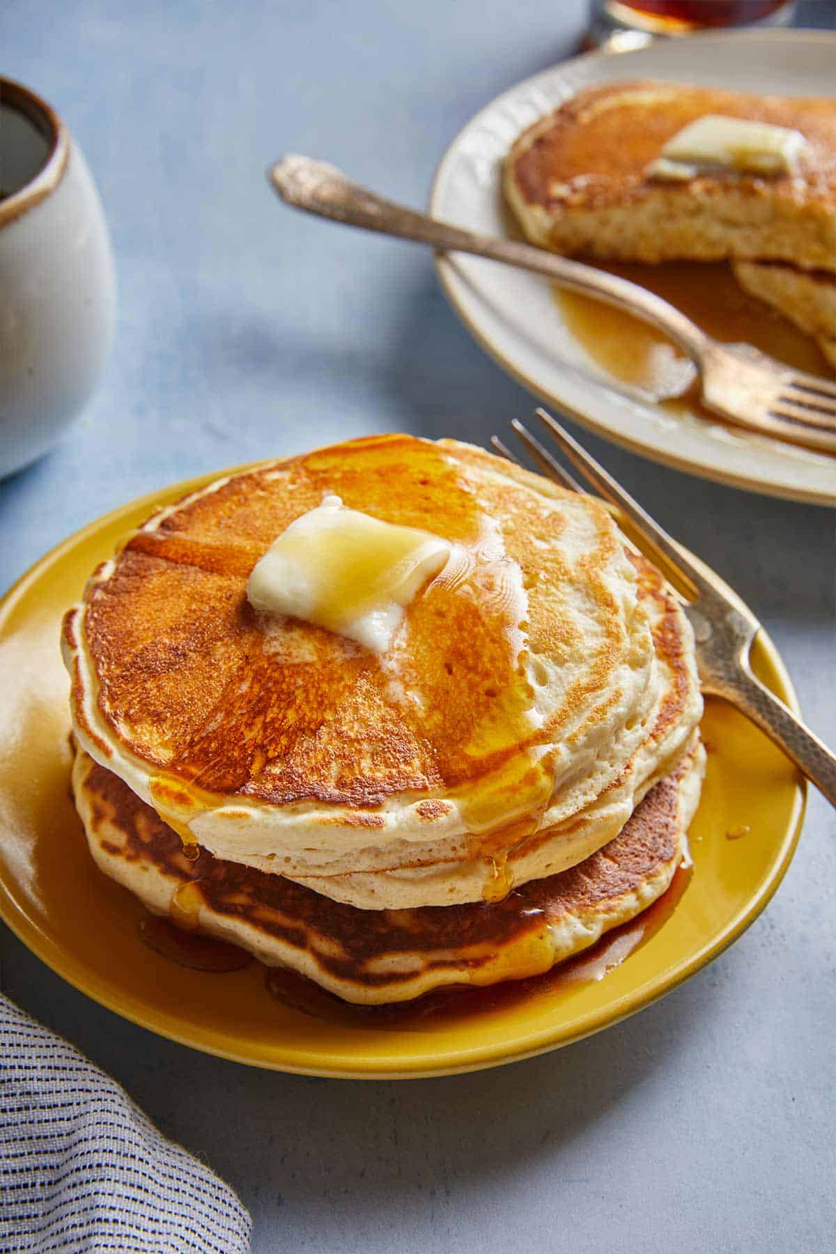 A stack of fluffy pancakes on a plate with maple syrup and butter on top.