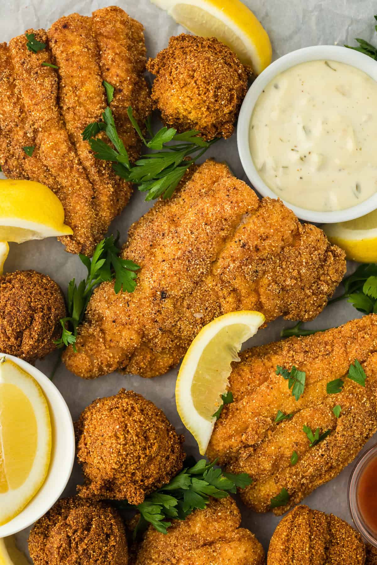 A close up of the best fried catfish with fried hush puppies on a white background with lemon wedges and parsley