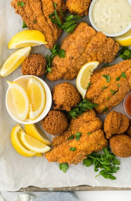 Deep fried catfish with hush puppies on a white surface with lemon wedges and parsley sprinkled on top