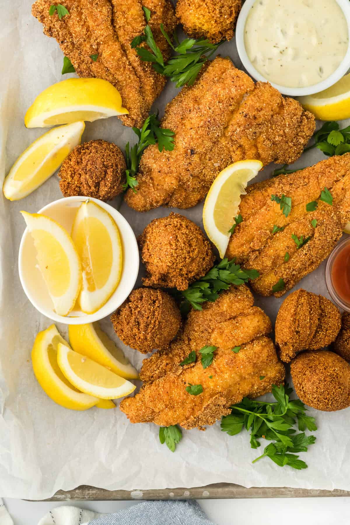 Deep fried catfish with hush puppies on a white surface with lemon wedges and parsley sprinkled on top