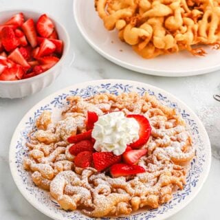 Funnel cake served up sprinkled with powdered sugar, whipped cream and fresh berries.