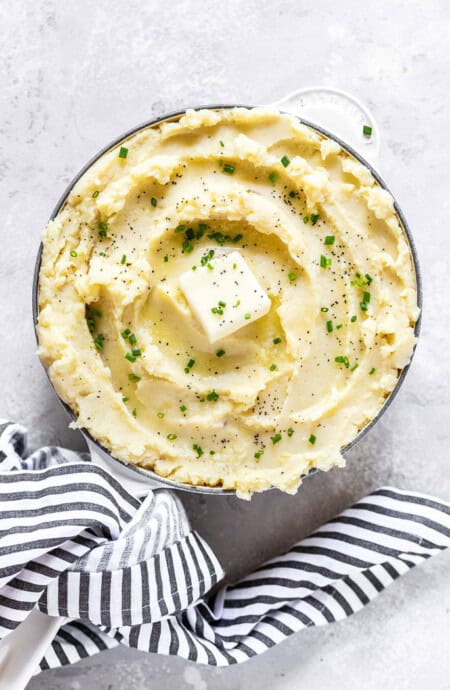 An overhead of a large bowl of creamy buttery Garlic Mashed Potatoes Recipe against a white background with striped napkin