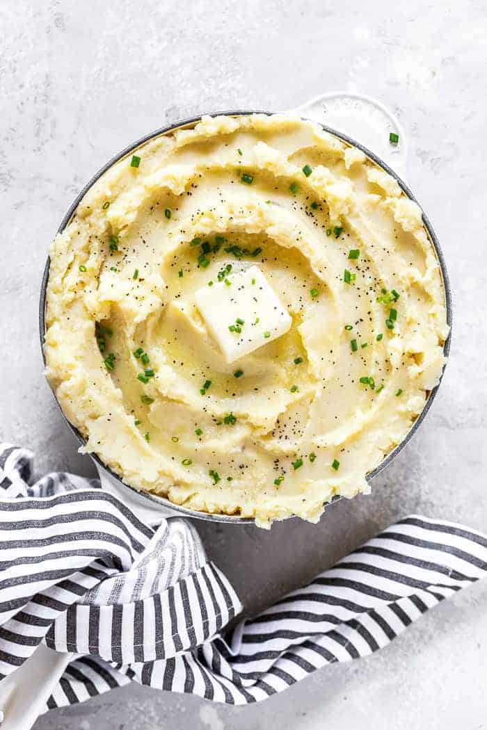 An overhead of a large bowl of creamy buttery Garlic Mashed Potatoes Recipe against a white background with striped napkin