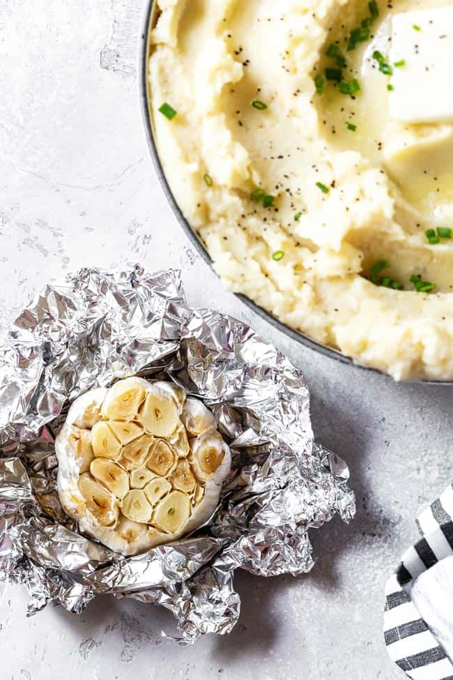 Roasted garlic in foil next to homemade garlic mashed potatoes recipe