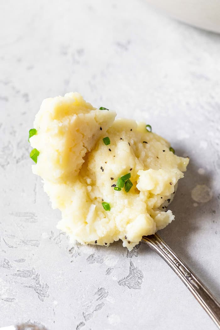 A spoon full of creamy garlic mashed potatoes recipe against a white gray background