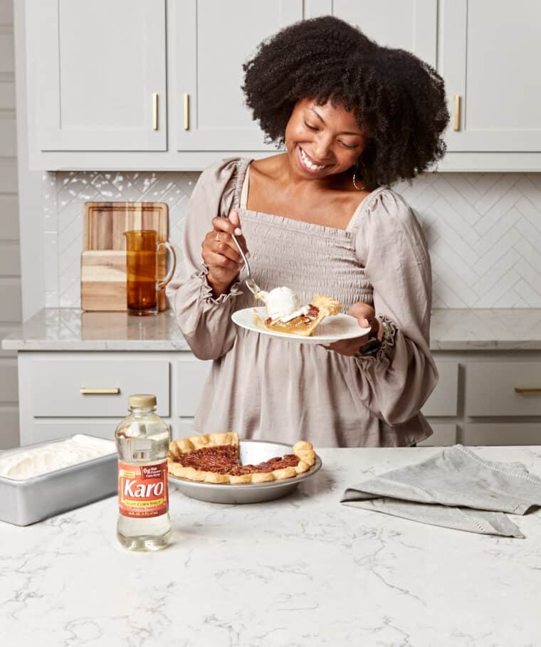 Woman holding a plate with a slice of pecan pie topped with ice cream.
