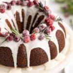 A close up of Gingerbread bundt cake with white glaze on white cake plate