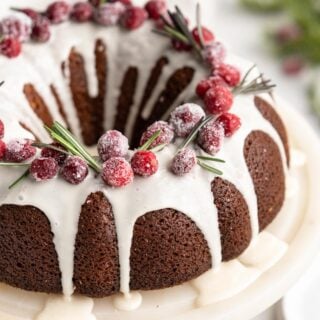A close up of Gingerbread bundt cake with white glaze on white cake plate