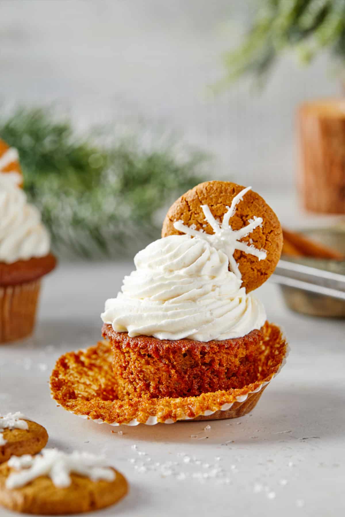 Gingerbread cupcake with the liner pulled back on the table with another cupcake and the pan in the background. 