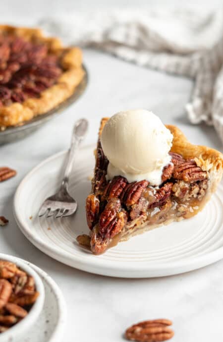 A scoop of vanilla ice cream melting over a slice of pecan pie.