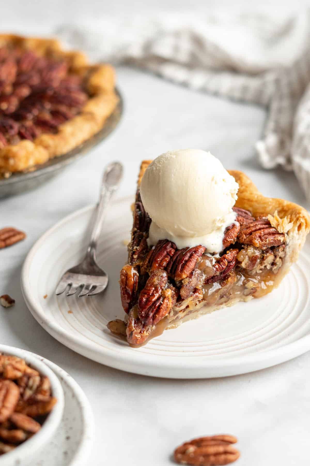 A scoop of vanilla ice cream melting over a slice of pecan pie.