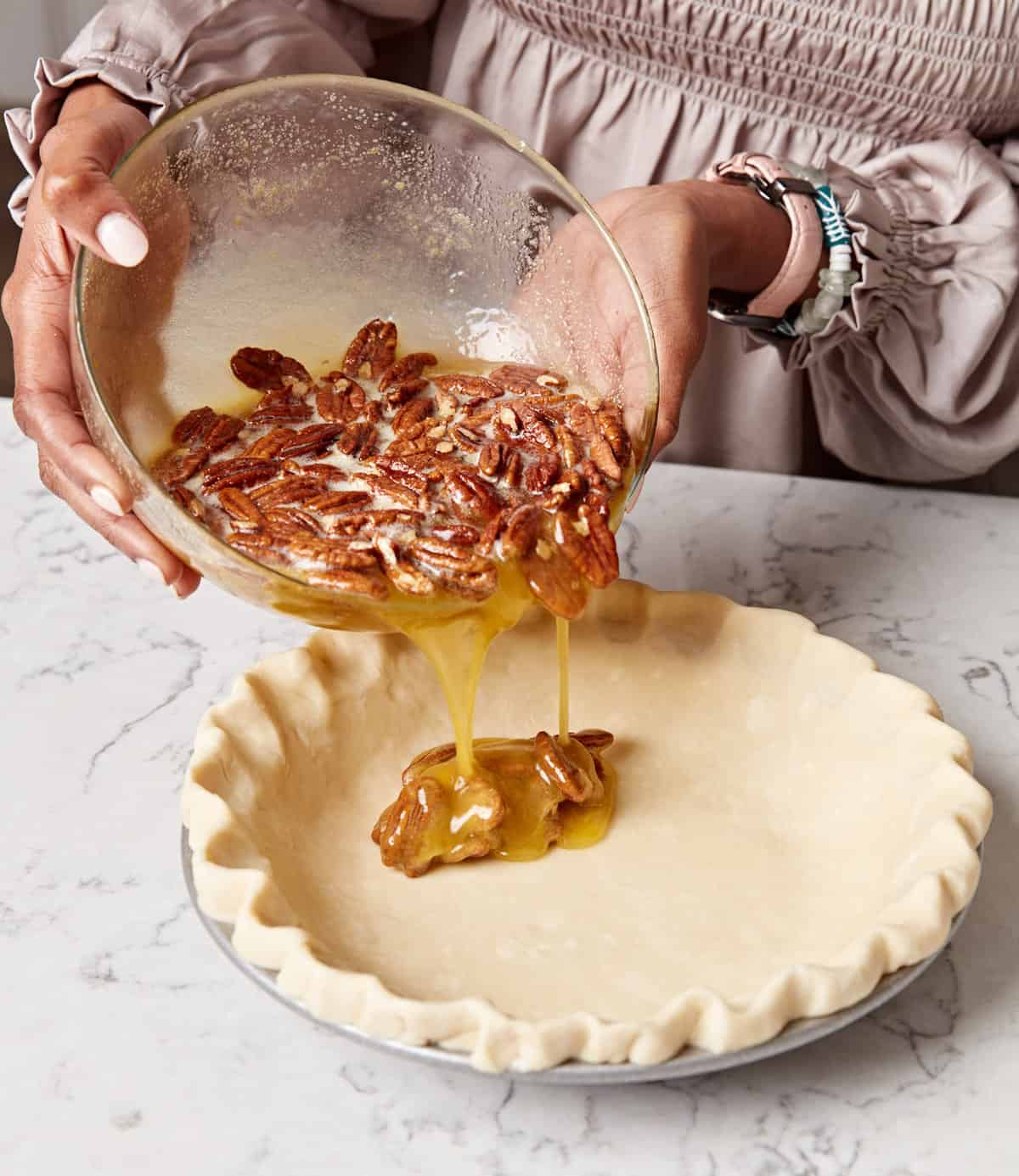 Woman pouring pecan pie filling from a bowl into a pie crust.