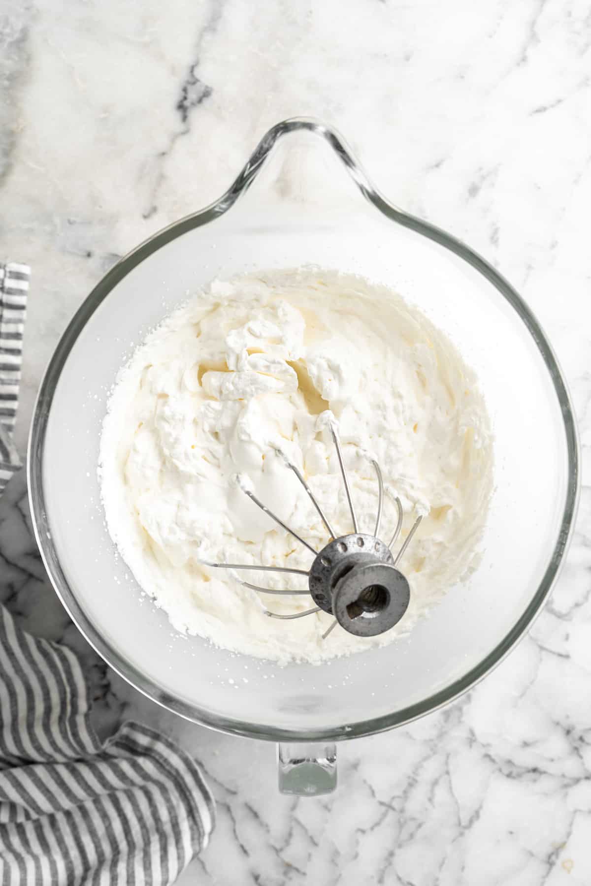 A stand mixer whisk in a bowl of vanilla ice cream.