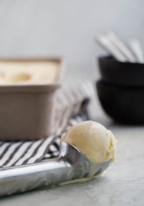 A large scoop of homemade vanilla ice cream slowly melting next to large vanilla bean ice cream container